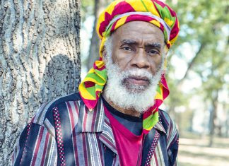 Things to do in Santa Cruz Israel Vibration reggae artist standing beside a tree in a colorful Rastafarian headwrap.