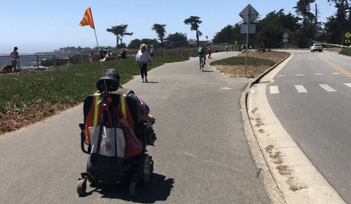 DANGER AFOOT A person using a mobility scooter travels along the West Cliff Drive path in Santa Cruz, separated from car traffic.