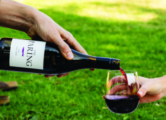 Crimson & Clover A bottle of The Paring red wine being poured into a glass outdoors on a green lawn.