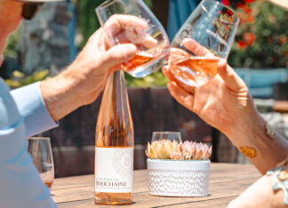Summer Swirls Two people toast glasses of Bouchaine Vin Gris of Pinot Noir beside a bottle on an outdoor table.