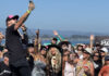 Things to do in Santa Cruz A singer performs in a crowd at an outdoor concert by the water as audience members raise their hands and take photos.