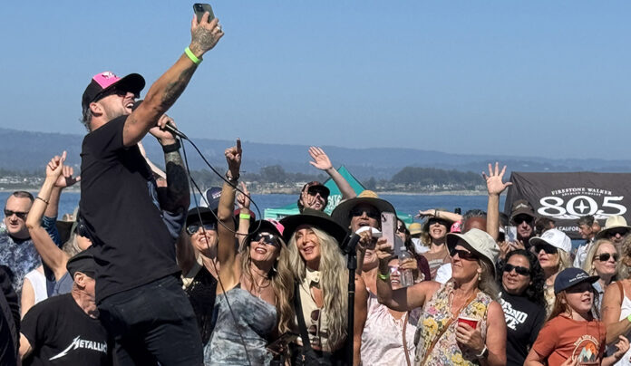 Things to do in Santa Cruz A singer performs in a crowd at an outdoor concert by the water as audience members raise their hands and take photos.