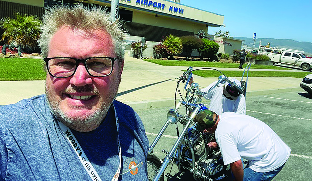 Tim Wood takes a selfie outside Woody’s at Watsonville Airport as a collectible motorcycle is moved inside.