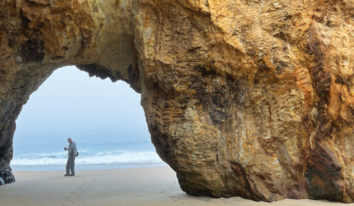 Don’t Be Blindsided A person stands beneath the Keyhole rock arch at Panther Beach near the ocean.