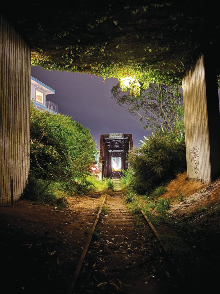 Night photo of railroad tracks leading through a dark, green-lit tunnel toward the San Lorenzo River and Santa Cruz Boardwalk.