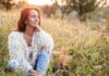 Shifting Hormones Woman sitting in a grassy field at sunset, representing wellness, reflection and conversations around menopause.