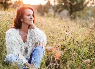 Shifting Hormones Woman sitting in a grassy field at sunset, representing wellness, reflection and conversations around menopause.