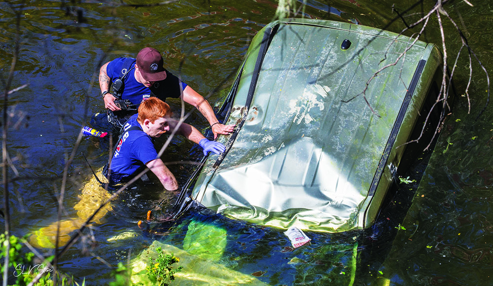 Firefighters work beside a partially submerged vehicle in Lompico Creek