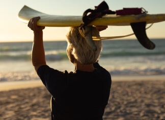 The Editor’s Desk Older surfer carrying a surfboard at the beach