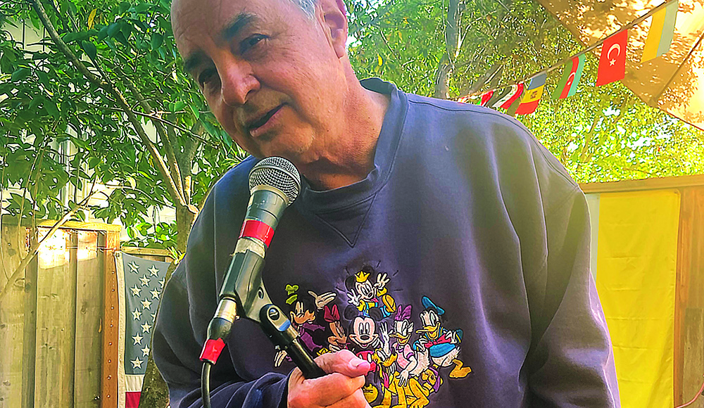 Kevin Keelan speaking into a microphone at a Seabright garden performance space