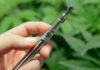 Safe Vapes? Cannabis vape pen held in front of marijuana plants