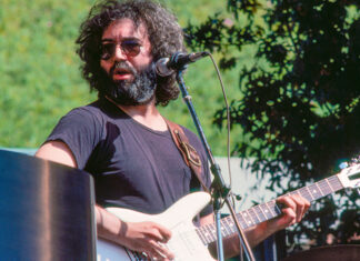 The Editor’s Desk Jerry Garcia playing a white electric guitar outdoors in 1976