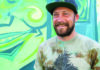 Brewing Up Art Shanty Shack co-owner Nathan Van Zandt standing in front of a colorful mural.
