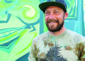 Brewing Up Art Shanty Shack co-owner Nathan Van Zandt standing in front of a colorful mural.