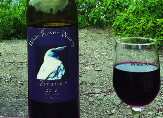 This Bird Flew Bottle of White Raven Winery 2016 Zinfandel beside a glass of red wine.