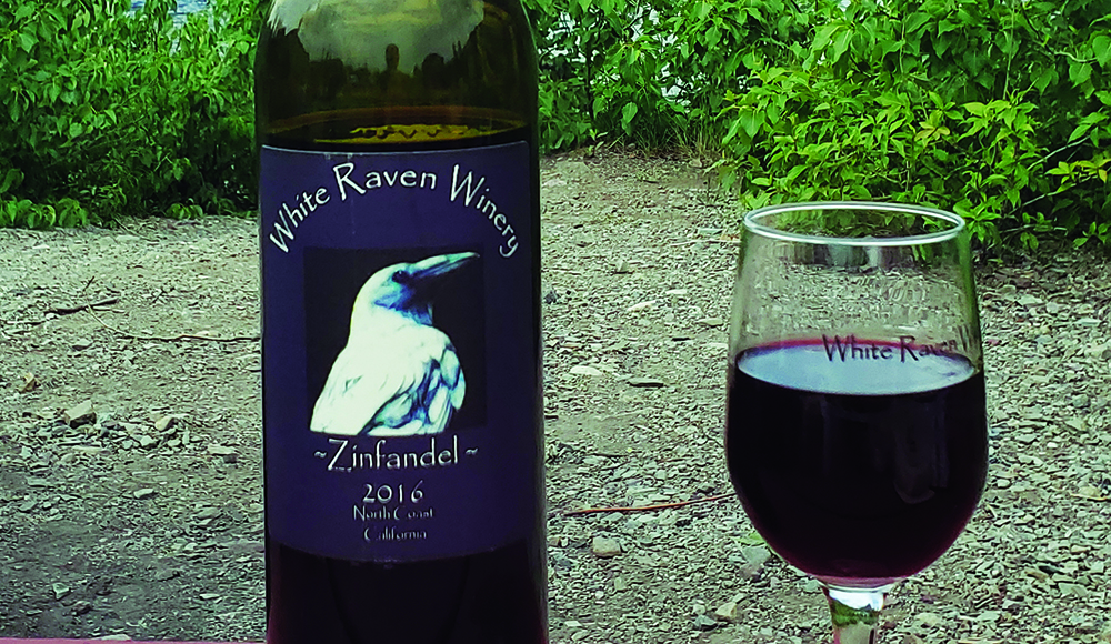 Bottle of White Raven Winery 2016 Zinfandel beside a glass of red wine.