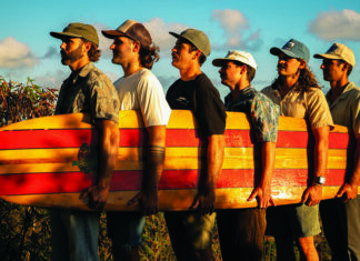 Things to do in Santa Cruz Twin Fin band members carrying a vintage surfboard outdoors.
