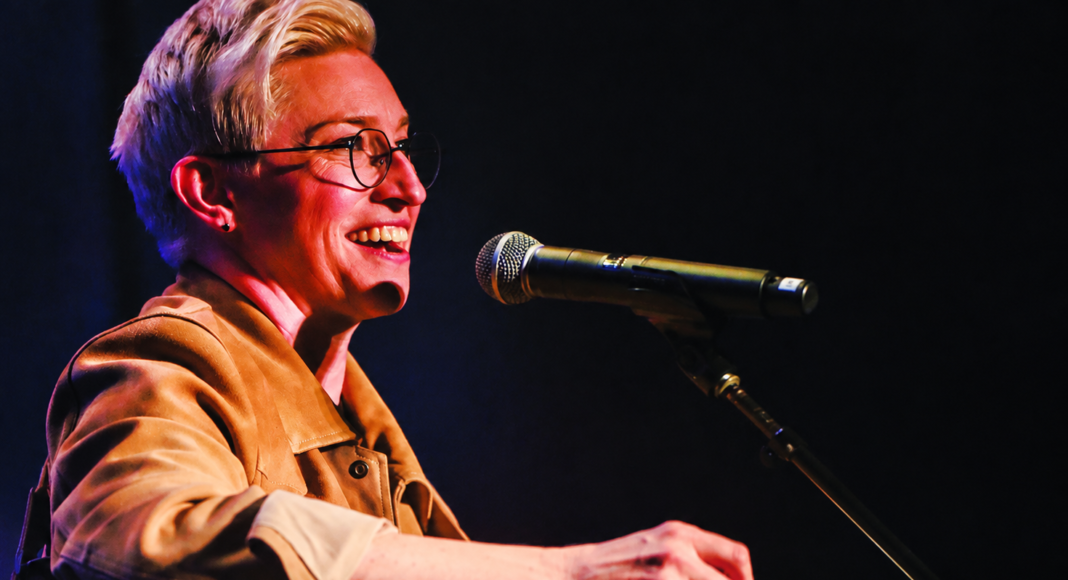 Comedian Kristin Key performs onstage with a guitar and microphone.