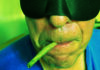 Cannabis for Sleep? Close-up of a person wearing a black sleep mask with a cannabis joint held in their mouth.