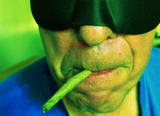 Cannabis for Sleep? Close-up of a person wearing a black sleep mask with a cannabis joint held in their mouth.