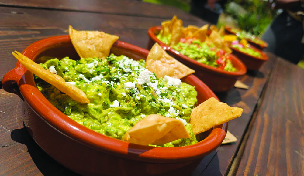 Bowls of fresh guacamole topped with cheese and herbs and surrounded by tortilla chips.