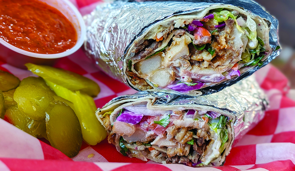 A Turkish döner wrap filled with meat, fries, lettuce, tomato, red cabbage and sauce, served with pickles and red sauce.