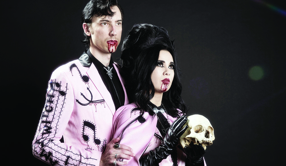 Twin Temple’s Alexandra and Zachary James pose in pink outfits with theatrical blood at their mouths, Alexandra holding a skull.