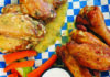 Catching Fire Chicken wings from Evil Wings served on blue-and-white checkered paper with carrot sticks, celery and a cup of dipping sauce.
