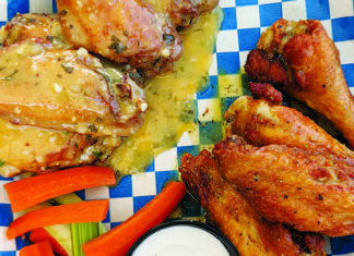 Catching Fire Chicken wings from Evil Wings served on blue-and-white checkered paper with carrot sticks, celery and a cup of dipping sauce.