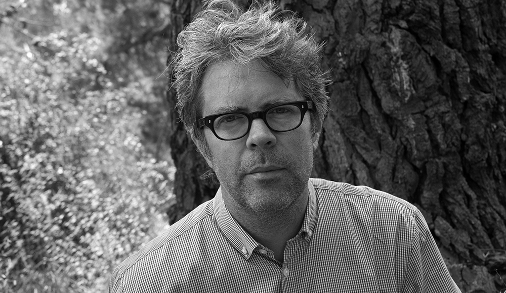 Jonathan Franzen in a black-and-white portrait beside a tree