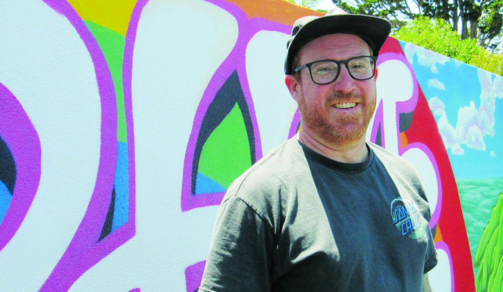 Artist Shaun Logan standing in front of one of his colorful murals.