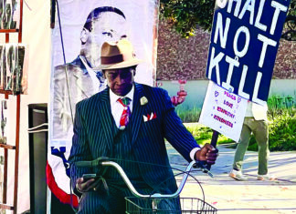 Driving Hope Santa Cruz humanitarian Curtis Reliford rides a bicycle while carrying a sign promoting peace, love, empathy and kindness.