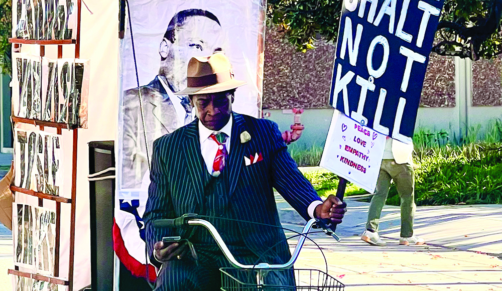 Santa Cruz humanitarian Curtis Reliford rides a bicycle while carrying a sign promoting peace, love, empathy and kindness.