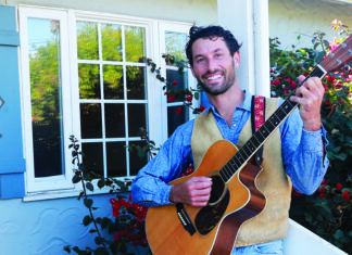 Rock the Porch Alt text: Santa Cruz Porchfest organizer Darrow Feldstein plays an acoustic guitar on a porch beside flowering roses.