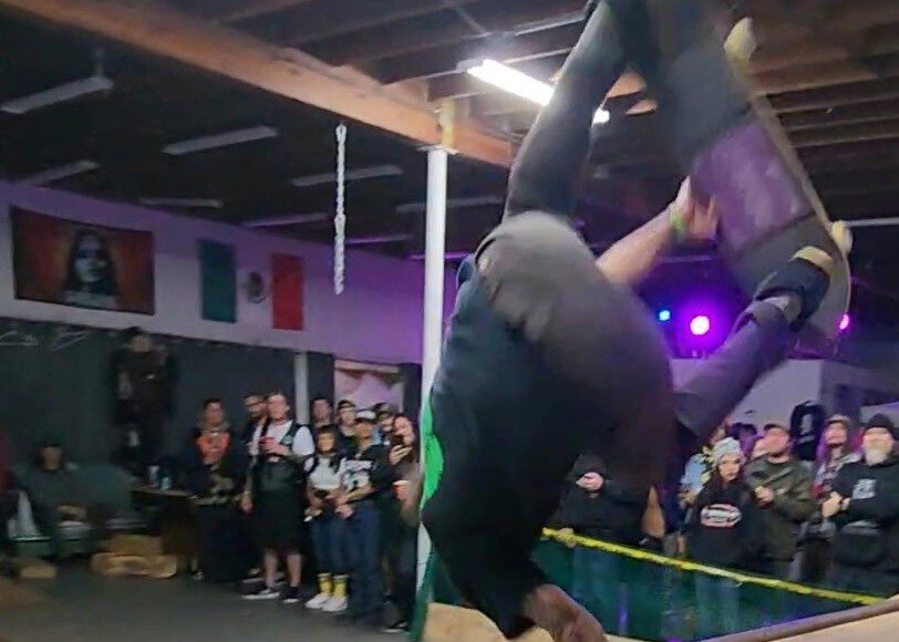 A skater goes inverted above a wooden ramp as spectators watch at a Grind the Cause benefit.