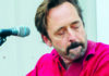 Things to do in Santa Cruz Michael Gaither in a bright red shirt beside a microphone, eyes closed.