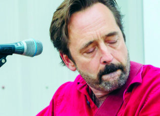 Things to do in Santa Cruz Michael Gaither in a bright red shirt beside a microphone, eyes closed.