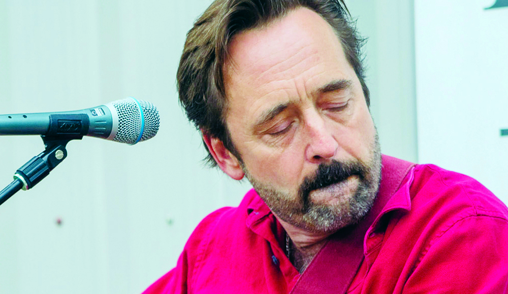Michael Gaither in a bright red shirt beside a microphone, eyes closed.