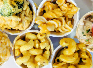 Dairy Departed Overhead view of six sample cups of vegan mac and cheese, with varied pasta shapes and toppings including broccoli and peppers.