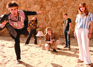 Smells Like Teen Spirit Five Coyote Theater band members pose on sand in front of a rocky bluff, with a camera and floor lamp as props.