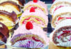 Happy Succession Rows of individual cake slices with chocolate topping, pink frosting, raspberries, strawberries and powdered sugar at Kelly’s French Bakery.