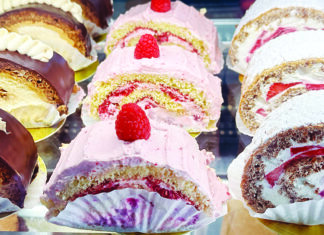 Happy Succession Rows of individual cake slices with chocolate topping, pink frosting, raspberries, strawberries and powdered sugar at Kelly’s French Bakery.