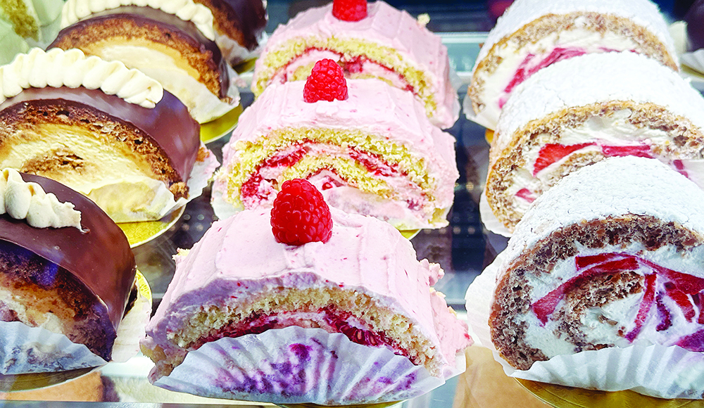 Rows of individual cake slices with chocolate topping, pink frosting, raspberries, strawberries and powdered sugar at Kelly’s French Bakery.