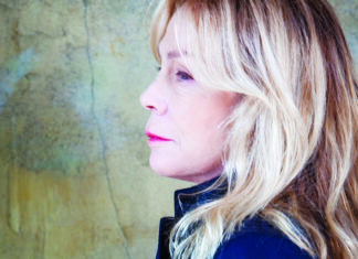 Things to do in Santa Cruz Rickie Lee Jones in profile, with long blonde hair and a dark jacket against a textured green wall.