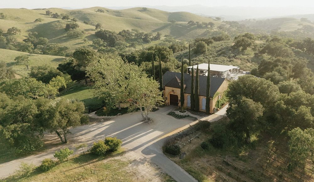 Aerial view of Demetria Estate’s buildings and courtyard surrounded by trees, vineyard rows and rolling green hills.