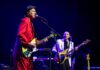 Crimson Roars in the Redwoods Adrian Belew sings and plays guitar in a red suit, with bassist Tony Levin behind him onstage.